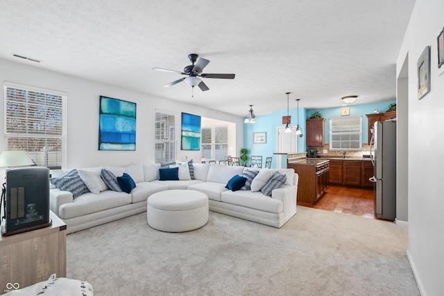 living room with ceiling fan, sink, a textured ceiling, and light colored carpet