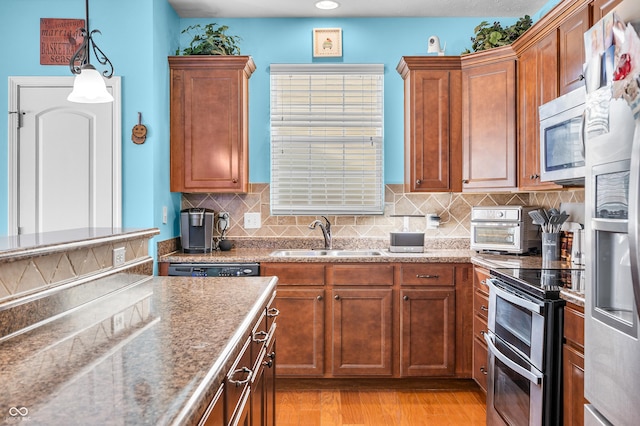 kitchen with hanging light fixtures, stainless steel appliances, light hardwood / wood-style floors, sink, and decorative backsplash