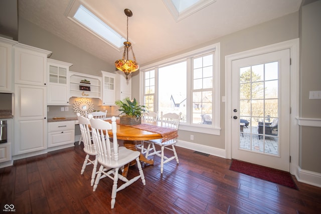 dining room featuring dark wood-type flooring, vaulted ceiling with skylight, baseboards, and visible vents