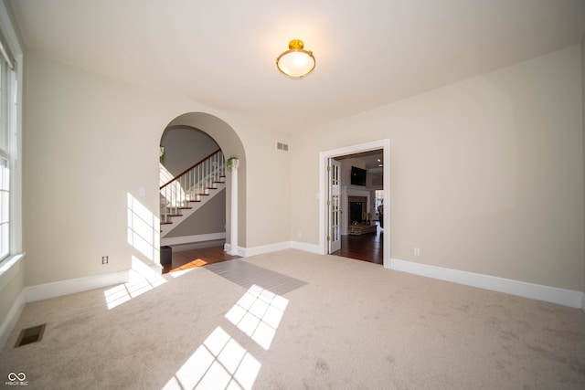 carpeted empty room with arched walkways, visible vents, a brick fireplace, and stairway