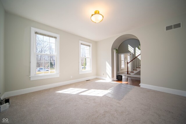 carpeted spare room featuring visible vents, arched walkways, baseboards, and stairway