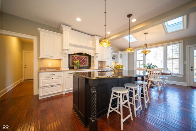 kitchen with vaulted ceiling with skylight, a breakfast bar area, dark wood finished floors, and white cabinetry