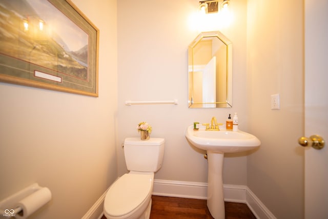 half bath featuring toilet, wood finished floors, baseboards, and a sink