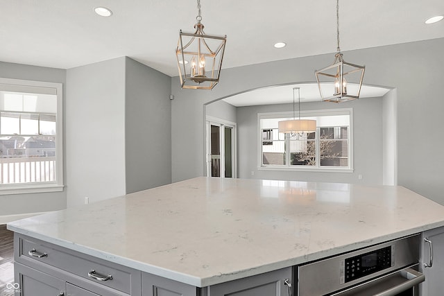 kitchen with gray cabinets, decorative light fixtures, light stone counters, and a center island