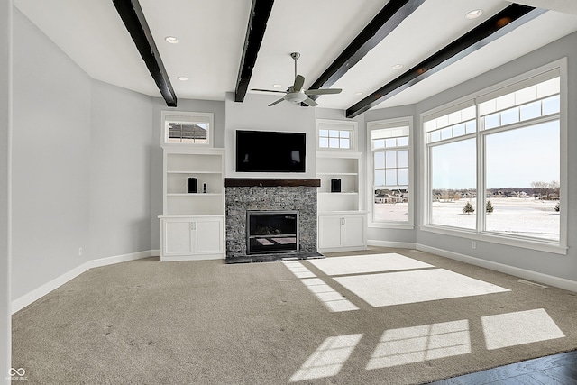 unfurnished living room with built in shelves, carpet floors, a stone fireplace, ceiling fan, and beam ceiling