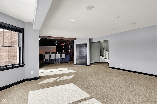 unfurnished living room featuring light colored carpet and bar