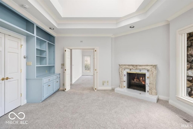 unfurnished living room featuring a raised ceiling, light carpet, and a high end fireplace