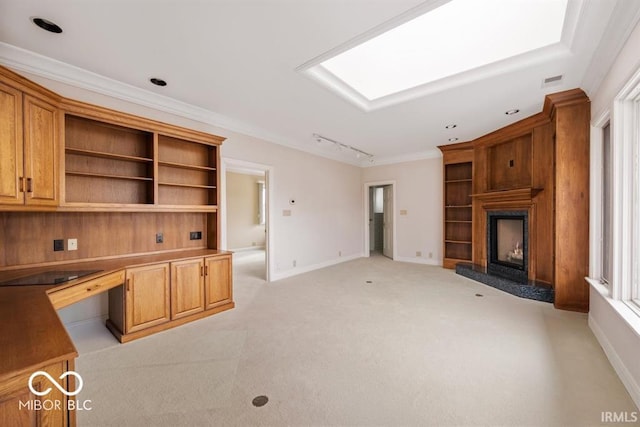 unfurnished living room featuring a fireplace, light colored carpet, ornamental molding, a skylight, and built in desk