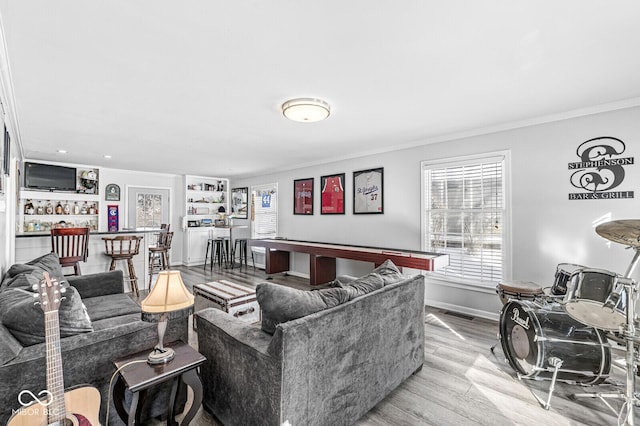 living room with light hardwood / wood-style flooring, crown molding, and bar area