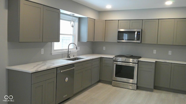 kitchen featuring stainless steel appliances, light hardwood / wood-style flooring, light stone countertops, sink, and gray cabinets