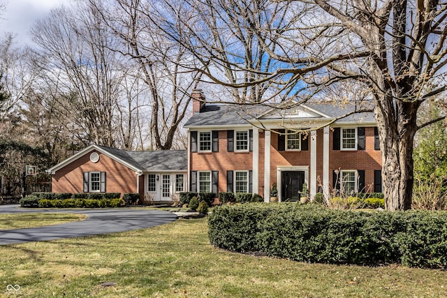 greek revival house with aphalt driveway, a front lawn, brick siding, and a chimney