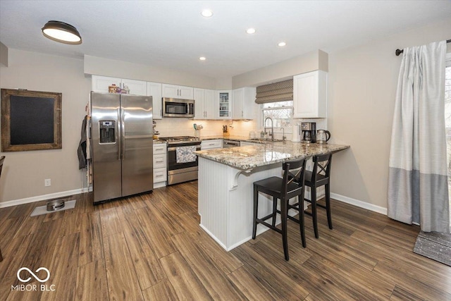 kitchen with a peninsula, a sink, decorative backsplash, stainless steel appliances, and white cabinetry