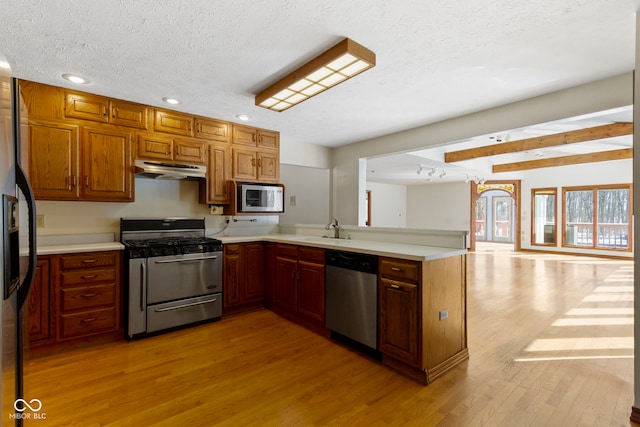 kitchen featuring light wood-type flooring, kitchen peninsula, stainless steel appliances, sink, and a textured ceiling