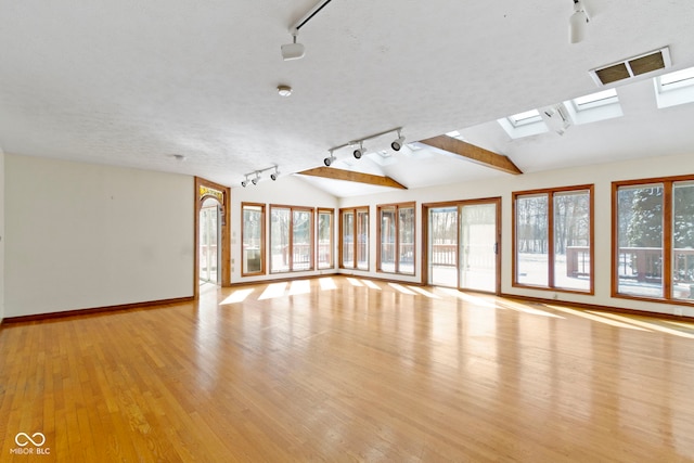 unfurnished living room with rail lighting, vaulted ceiling with skylight, and light hardwood / wood-style floors