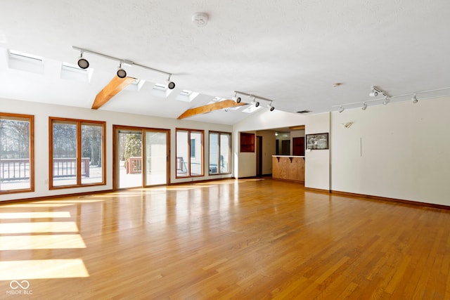 spare room with track lighting, light hardwood / wood-style flooring, a textured ceiling, and lofted ceiling with skylight