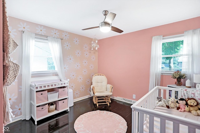 bedroom with ceiling fan, a nursery area, and dark wood-type flooring