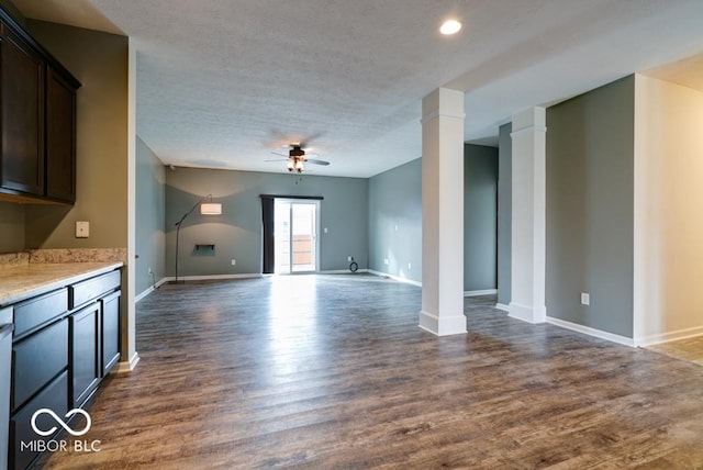 unfurnished living room with baseboards, dark wood-style floors, ceiling fan, a textured ceiling, and ornate columns