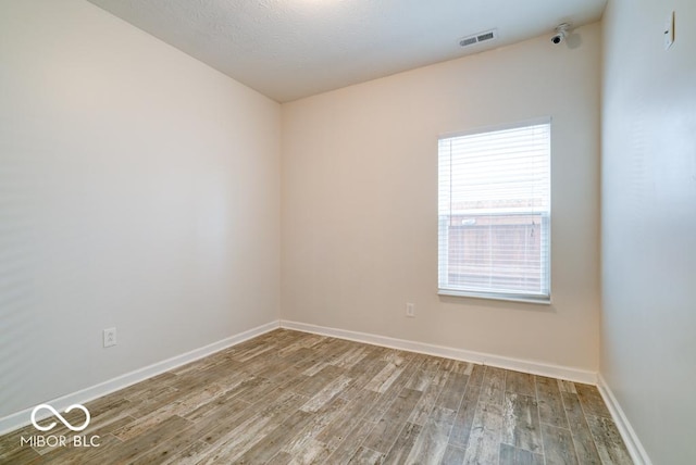 unfurnished room featuring baseboards, visible vents, and wood finished floors