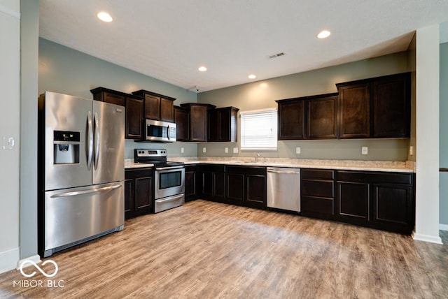 kitchen with stainless steel appliances, dark brown cabinets, light wood-style flooring, and recessed lighting