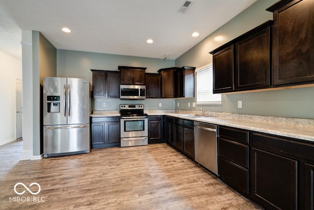 kitchen featuring dark brown cabinetry, visible vents, light wood-style flooring, appliances with stainless steel finishes, and a sink