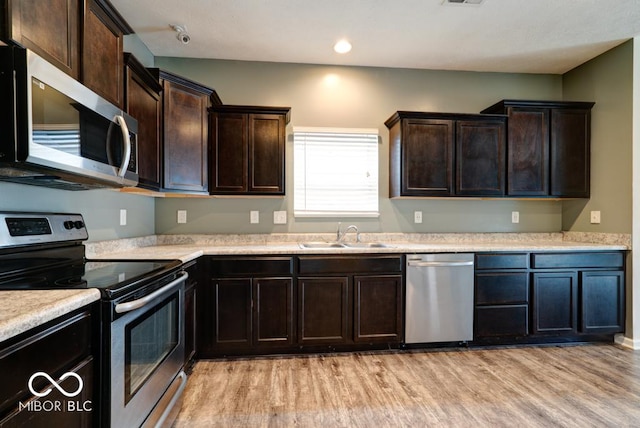 kitchen featuring dark brown cabinetry, light wood-style flooring, stainless steel appliances, light countertops, and a sink