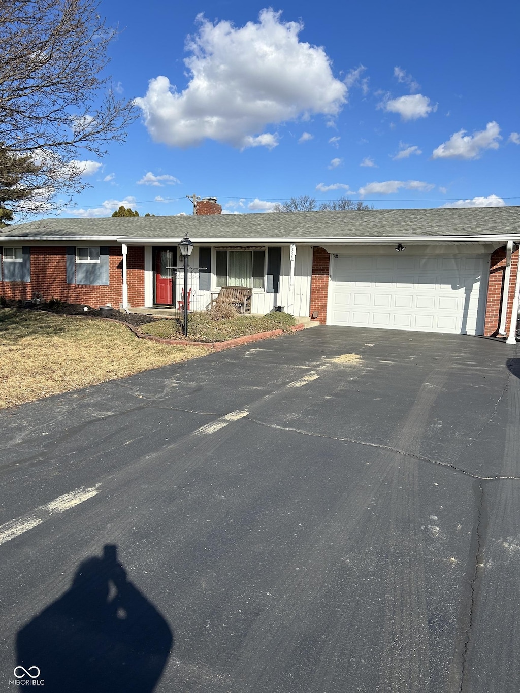 ranch-style house with a porch, aphalt driveway, an attached garage, brick siding, and roof with shingles