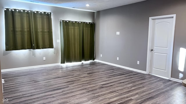 spare room featuring a textured ceiling, baseboards, and dark wood-type flooring