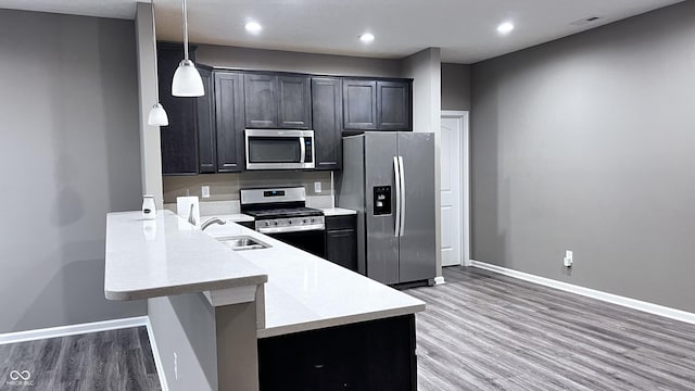 kitchen featuring appliances with stainless steel finishes, decorative light fixtures, a peninsula, light countertops, and a sink