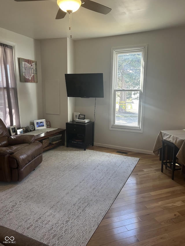 living room with wood-type flooring, visible vents, ceiling fan, and baseboards