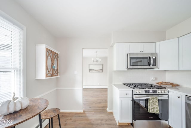 kitchen with light wood finished floors, light countertops, backsplash, appliances with stainless steel finishes, and white cabinets