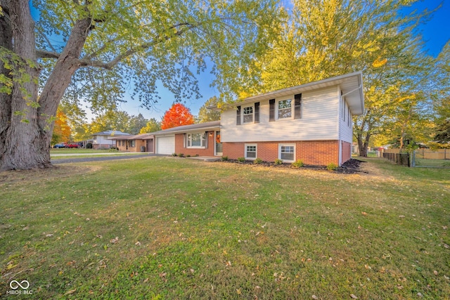 split level home featuring aphalt driveway, an attached garage, brick siding, fence, and a front lawn