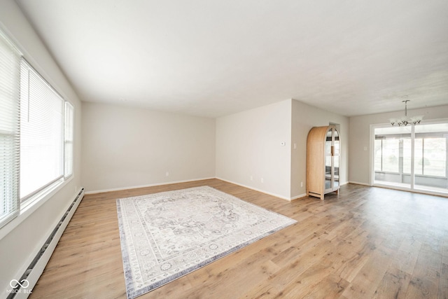 empty room featuring arched walkways, a notable chandelier, light wood finished floors, and baseboard heating