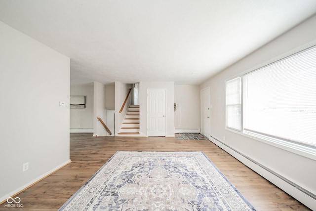 empty room with a baseboard heating unit, stairs, baseboards, and wood finished floors