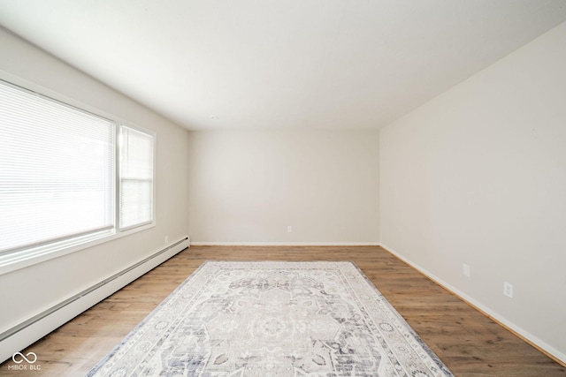 empty room with a baseboard radiator, baseboards, and wood finished floors