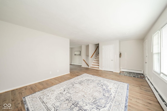 living area with a baseboard heating unit, stairway, and light wood-style floors