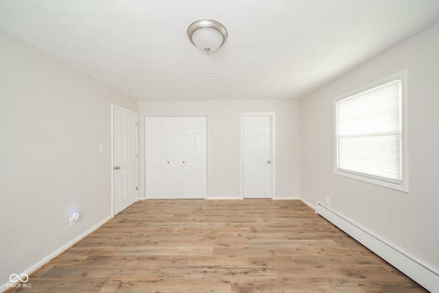 unfurnished bedroom featuring baseboards, baseboard heating, a closet, and light wood-style floors