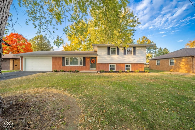 tri-level home featuring a garage, aphalt driveway, a front lawn, and brick siding