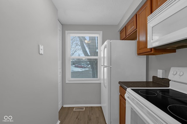 kitchen with white appliances, wood finished floors, visible vents, brown cabinetry, and dark countertops