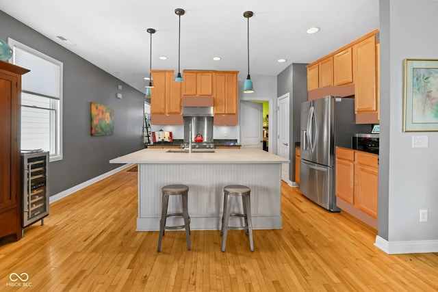 kitchen featuring a center island with sink, hanging light fixtures, light hardwood / wood-style flooring, stainless steel fridge, and wine cooler