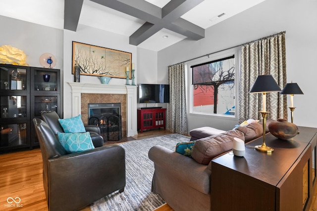 living room featuring coffered ceiling, a tiled fireplace, beam ceiling, and wood-type flooring