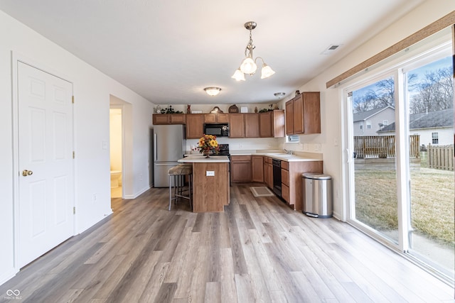 kitchen featuring a wealth of natural light, a center island, black appliances, and light wood-type flooring