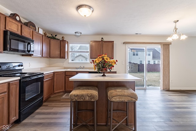 kitchen with a kitchen bar, light countertops, dark wood-style floors, black appliances, and a sink