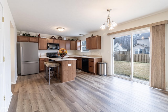 kitchen with light wood finished floors, a center island, black appliances, and light countertops