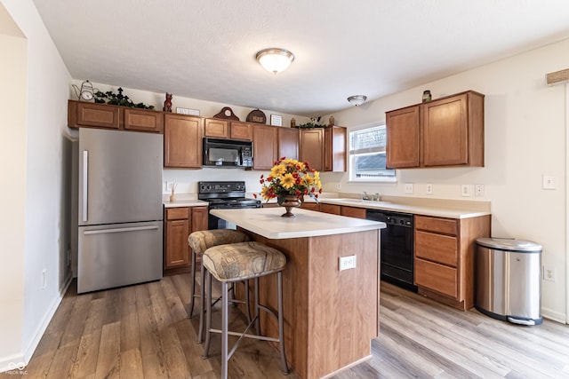 kitchen featuring black appliances, a breakfast bar area, light countertops, and light wood finished floors