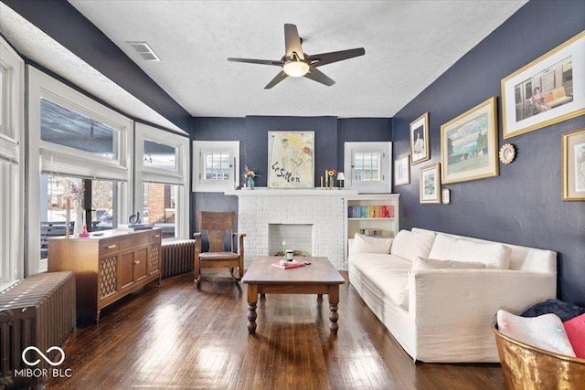 living room with radiator, a textured ceiling, a brick fireplace, and dark hardwood / wood-style floors