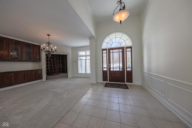 foyer entrance with light colored carpet, crown molding, ornate columns, and light tile patterned flooring