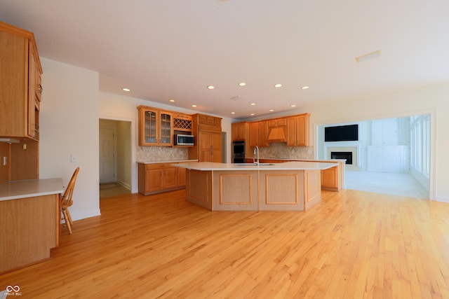 kitchen featuring a sink, light countertops, appliances with stainless steel finishes, an island with sink, and glass insert cabinets