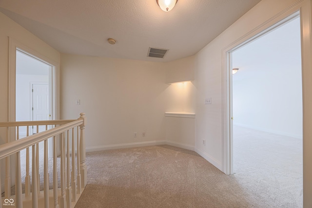 hall featuring baseboards, visible vents, a textured ceiling, and light colored carpet