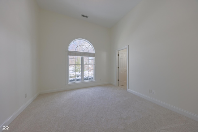 spare room with baseboards, a high ceiling, visible vents, and light colored carpet