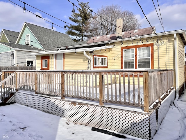 snow covered rear of property with a chimney and a wooden deck